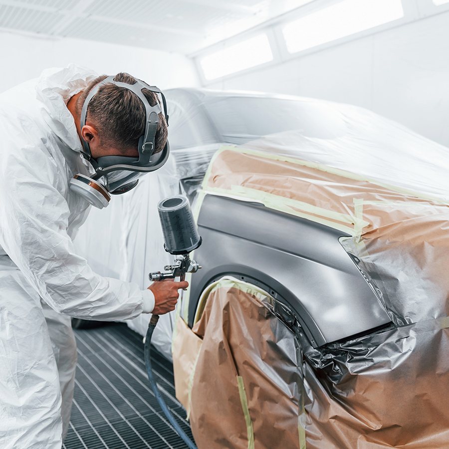 A technician in full protective gear spraying a masked fender inside the CBS paint booth