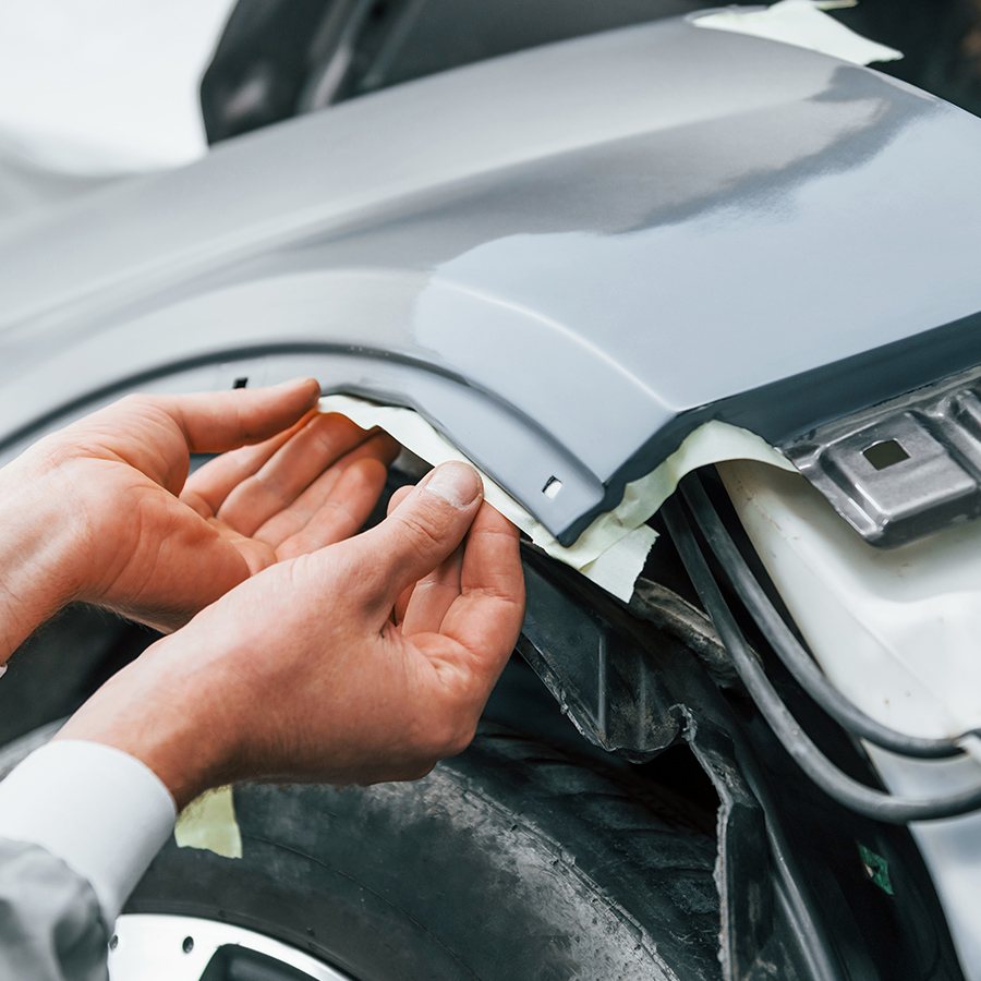 Hands checking a panel gap on a primed fender